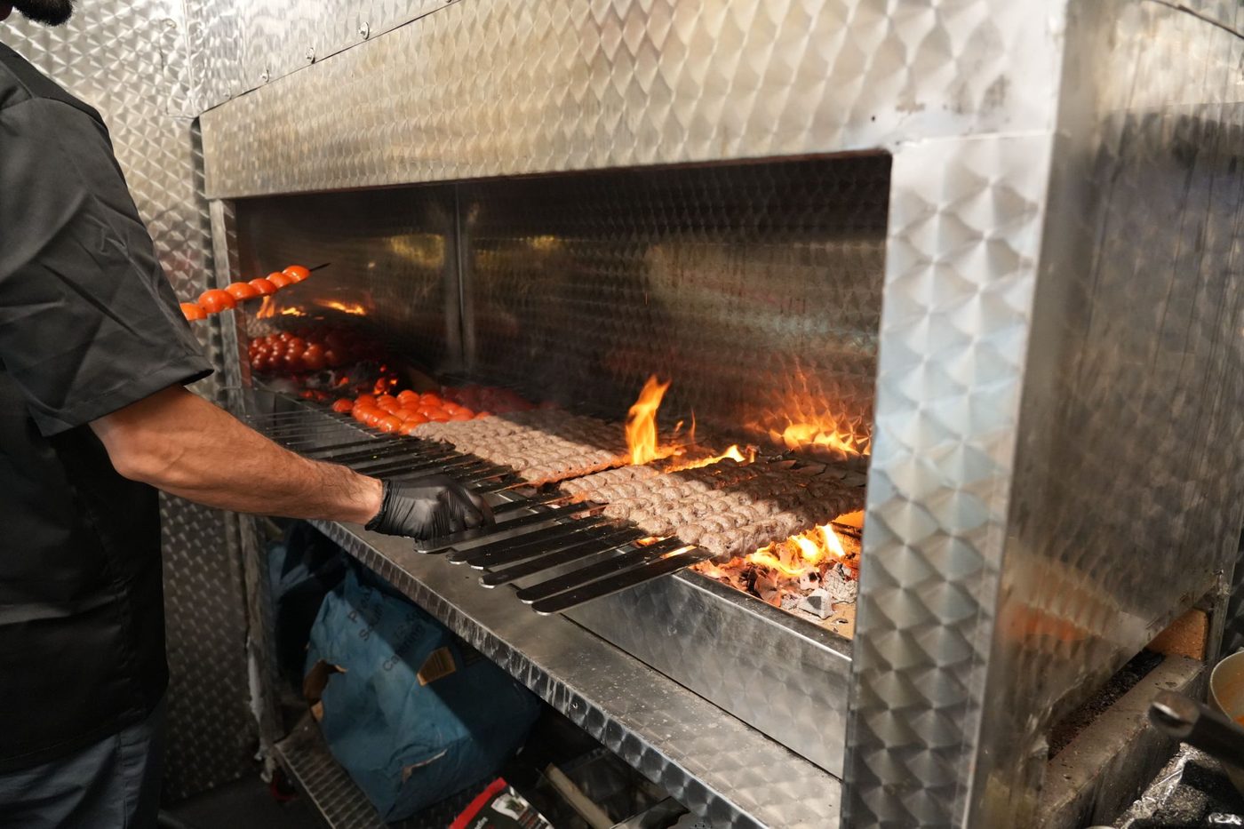 Chef grilling kebabs over the charcoal fire at H & H